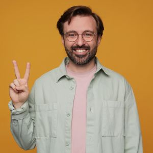 indoor-portrait-handsome-bearded-male-posing-orange-background-showing-v-gesture-into-camera-with-positive-happy-facial-expression_295783-16722