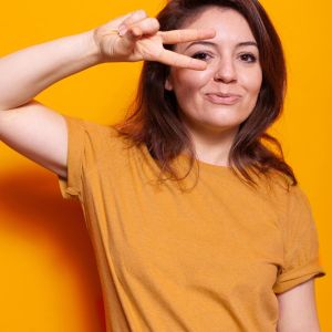 portrait-cheerful-woman-making-peace-sign-with-two-fingers-studio-positive-person-smiling-doing-optimistic-victory-symbol-while-looking-camera-orange-background_482257-38127